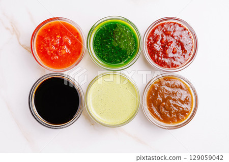 Colorful assortment of sauces in glass jars on white background Colorful assortment of sauces in glass jars on white background 129059042