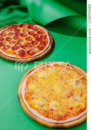 Delicious pepperoni and cheese pizzas on vibrant green background 129059489