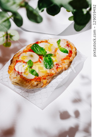 Freshly baked pizza with basil and mozzarella on a light background Freshly baked pizza with basil and mozzarella on a light background 129059492