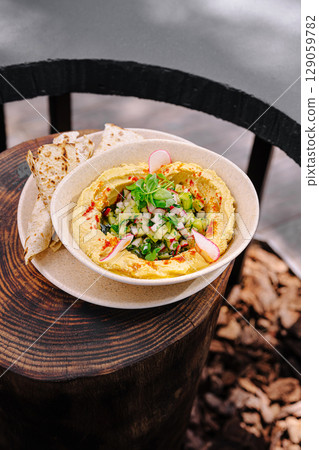 Creamy hummus topped with fresh vegetables served on a rustic table 129059782