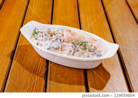 Gourmet seafood dish served in white ceramic bowl on wooden table Gourmet seafood dish served in white ceramic bowl on wooden table 129059804