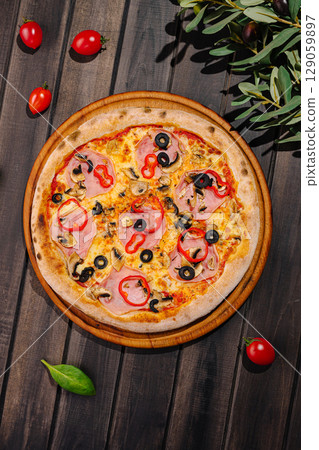 Delicious pizza topped with ham, olives, and bell peppers on wooden table 129059897