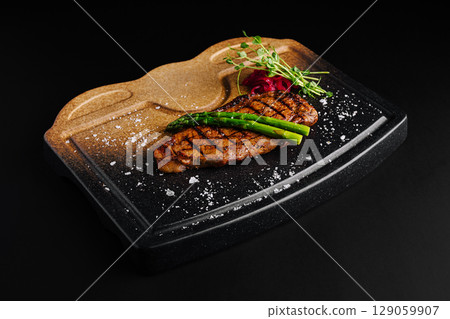 Savory grilled steak served on a stylish black platter with garnishes 129059907