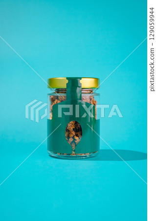 Glass jar filled with granola and a spoon against a vibrant turquoise background 129059944