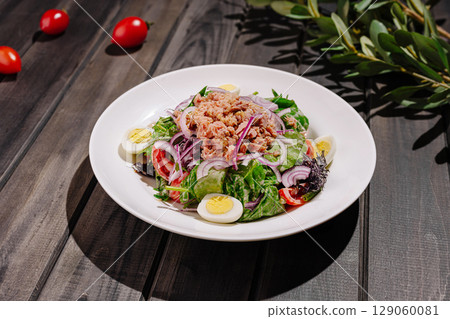 Fresh salad with tuna, eggs, and vegetables on wooden table 129060081