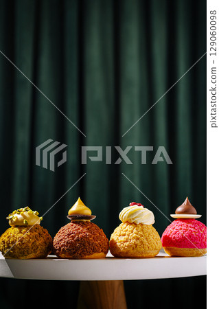 Four colorful pastries displayed on a table against a dark curtain backdrop 129060098