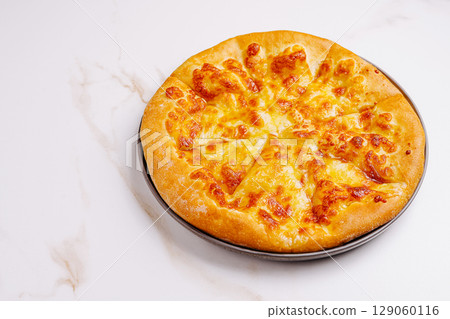Cheese pizza on a black plate placed on a white marble surface 129060116