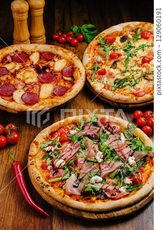 Delicious variety of pizzas displayed on wooden boards in a cozy restaurant Delicious variety of pizzas displayed on wooden boards in a cozy restaurant 129060191