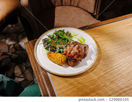 Delicious grilled steak with corn and salad at a cozy restaurant setting Delicious grilled steak with corn and salad at a cozy restaurant setting 129060195