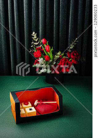 Gift box featuring heart-shaped treat with flowers in background 129060233