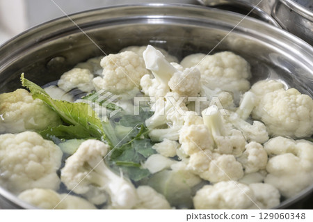 Fresh cauliflower is boiled in a saucepan with water. The vegetable is divided into florets and boiled in a saucepan. 129060348