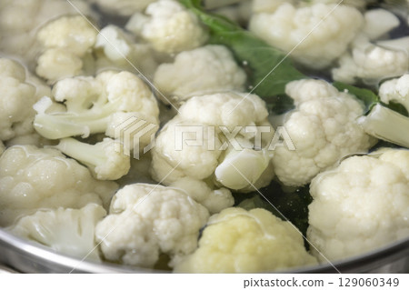 Fresh cauliflower is boiled in a saucepan with water. The vegetable is divided into florets and boiled in a saucepan. 129060349