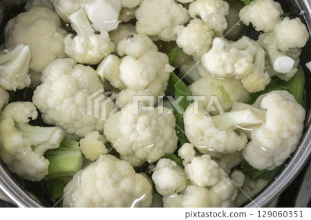 Fresh cauliflower is boiled in a saucepan with water. The vegetable is divided into florets and boiled in a saucepan. 129060351
