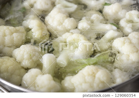 Fresh cauliflower is boiled in a saucepan with water. The vegetable is divided into florets and boiled in a saucepan. 129060354