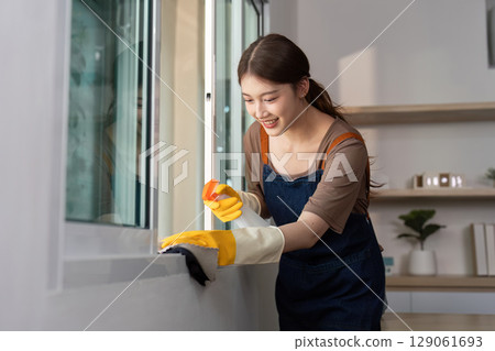 Home Cleaning. Young woman joyfully cleaning window with spray and cloth. Home Cleaning. Young woman joyfully cleaning window with spray and cloth. 129061693