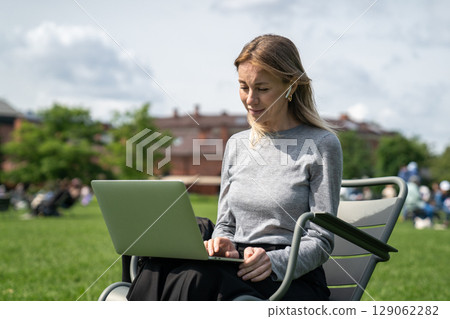 Concentrated woman using laptop in green park, connecting video call conference online, remote job Concentrated woman using laptop in green park, connecting video call conference online, remote job 129062282