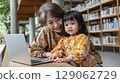 Grandmother and granddaughter enjoying learning together at a library with laptop and books 129062729