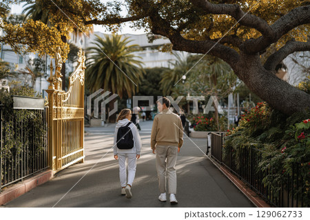 Students walking together through a school garden pathway surrounded by lush greenery and trees 129062733