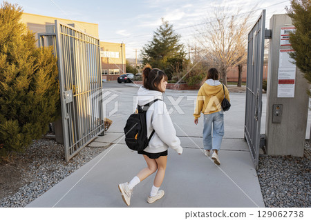 Two young women walking through school gates, ready for back to school season with backpacks 129062738