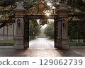 Grand entrance gate of a prestigious school with lush greenery and sunlight illuminating the pathway 129062739