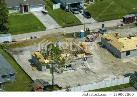 Professional builders working on roof construction of unfinished suburban home with wooden frame structure in Florida rural area. Concept of housing development in America 129062800