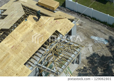 Professional builders working on roof construction of unfinished suburban home with wooden frame structure in Florida rural area. Concept of housing development in America 129062801