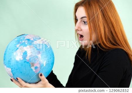 Portrait of a sad worried young woman holding geographic globe of the world in her hands. Travel destination and planet protection concept. 129062832