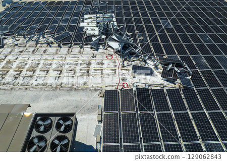 Photovoltaic solar panels destroyed by hurricane strong wind mounted on industrial building roof for producing green ecological electricity. Consequences of natural disaster in Florida Photovoltaic solar panels destroyed by hurricane strong wind mounted on industrial building roof for producing green ecological electricity. Consequences of natural disaster in Florida 129062843