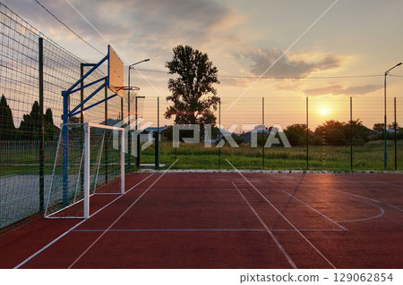 Outdoors mini football and basketball court with ball gate and basket surrounded with high protective fence. 129062854