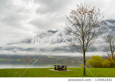 Moody autumn landscape with bare tree and lonely bench on mountain lake shore. Moody autumn landscape with bare tree and lonely bench on mountain lake shore. 129062881