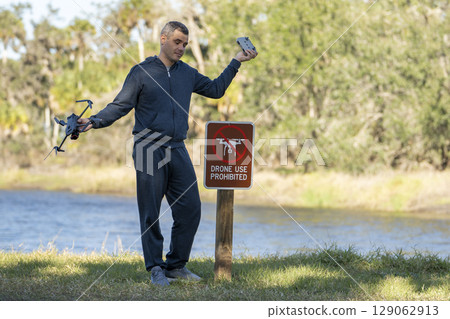 Man is sad that he is not allowed to fly his quadcopter state park no drone area. Operator is unauthorised to use UAS near restriction sign 129062913