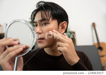 Self-Care: Young Man Checking Skin with Mirror 129063057