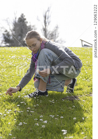 Young woman picking daisies in sunny park Young woman picking daisies in sunny park 129063222