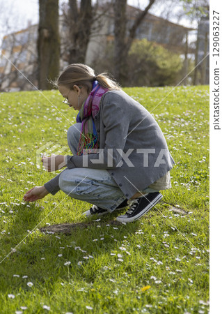 Girl picking daisies in a field on a bright spring day Girl picking daisies in a field on a bright spring day 129063227