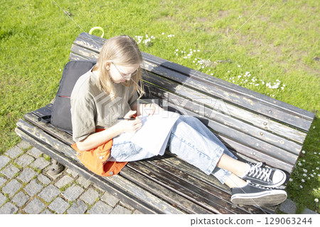 Student girl writing outdoors on park bench on sunny day Student girl writing outdoors on park bench on sunny day 129063244