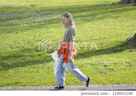 Teenage girl walking in park carrying closed umbrella on sunny day 129063290