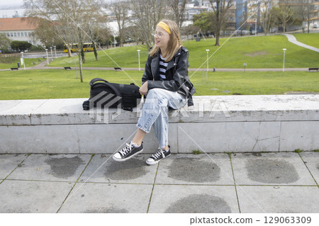 Young student smiling sitting on a wall in a park with backpack Young student smiling sitting on a wall in a park with backpack 129063309