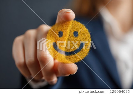 A businesswoman touches a virtual yellow smiley face, symbolizing positivity, feedback, and customer satisfaction. Modern concept for happiness, service, or workplace morale 129064055