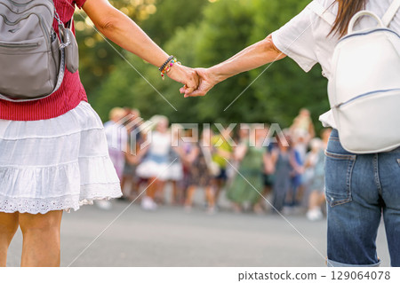 Close-up of two women holding hands, backs turned to camera, traditional Bulgarian horo dance. Concept of horo as cultural bond, shared heritage, symbol of unity, friendship Close-up of two women holding hands, backs turned to camera, traditional Bulgarian horo dance. Concept of horo as cultural bond, shared heritage, symbol of unity, friendship 129064078