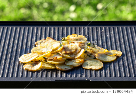 sliced potatoes with oil on hot grill pan 129064484