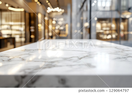A crisp, white marble tabletop with grey veining in the foreground, against a blurred background of a brightly lit shopping mall with store displays. 129064797