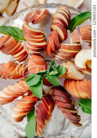 Sliced peaches with mint leaves decorating a glass plate 129065105