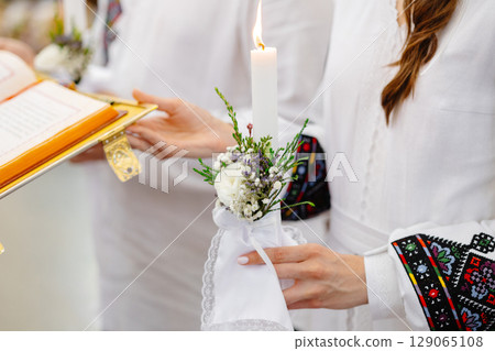 Woman holding burning candle decorated with flowers during religious ceremony 129065108