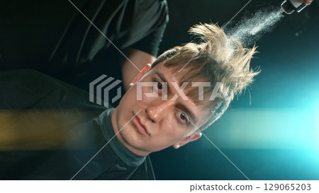 Young Man with Beard at Barber Shop. Barber is Preparing his Haircut. Dark Atmosphere, Black Background. Concept of Barber and a Client. Young Man with Beard at Barber Shop. Barber is Preparing his Haircut. Dark Atmosphere, Black Background. Concept of Barber and a Client. 129065203