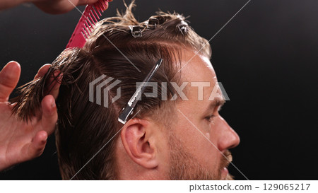 Young Man with Beard at Barber Shop. Barber is Preparing his Haircut. Dark Atmosphere, Black Background. Concept of Barber and a Client. 129065217