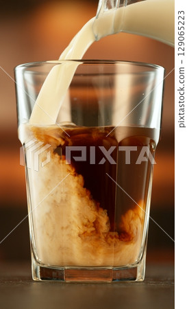 Refreshing coffee with pouring milk into glass, close-up Refreshing coffee with pouring milk into glass, close-up 129065223