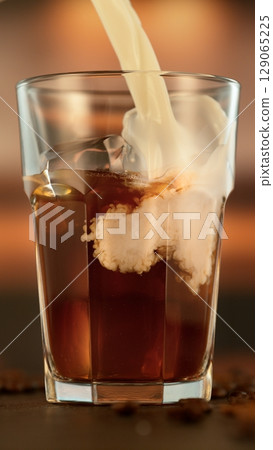 Refreshing coffee with pouring milk into glass, close-up Refreshing coffee with pouring milk into glass, close-up 129065225