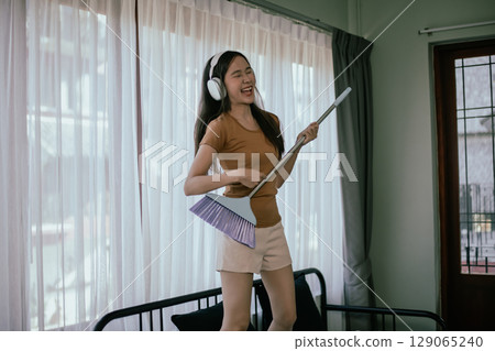 Asian woman dancing while cleaning in the house. 129065240