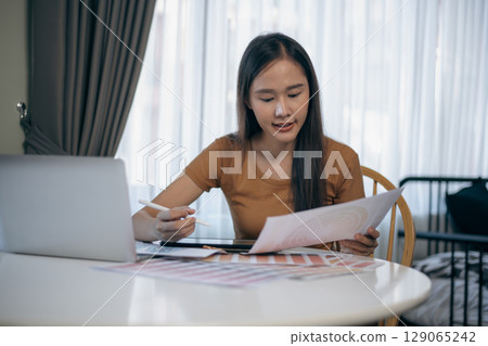 Asian woman designing clothes with laptop at home. Asian woman designing clothes with laptop at home. 129065242
