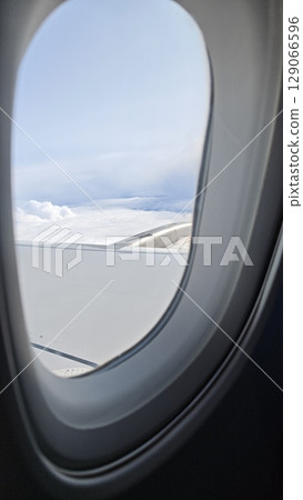 View from airplane window showing aircraft wing above white clouds under a blue sky 129066596